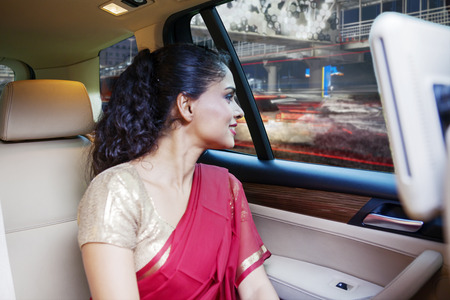 121632708-indian-woman-wearing-saree-clothes-while-looking-out-through-the-window-and-sitting-backseat-in-a-ca
